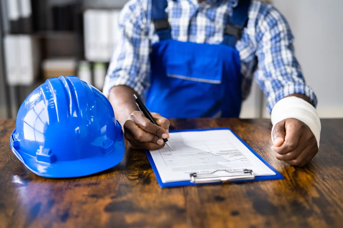 Injured worker completing a claim form, hard hat on the table