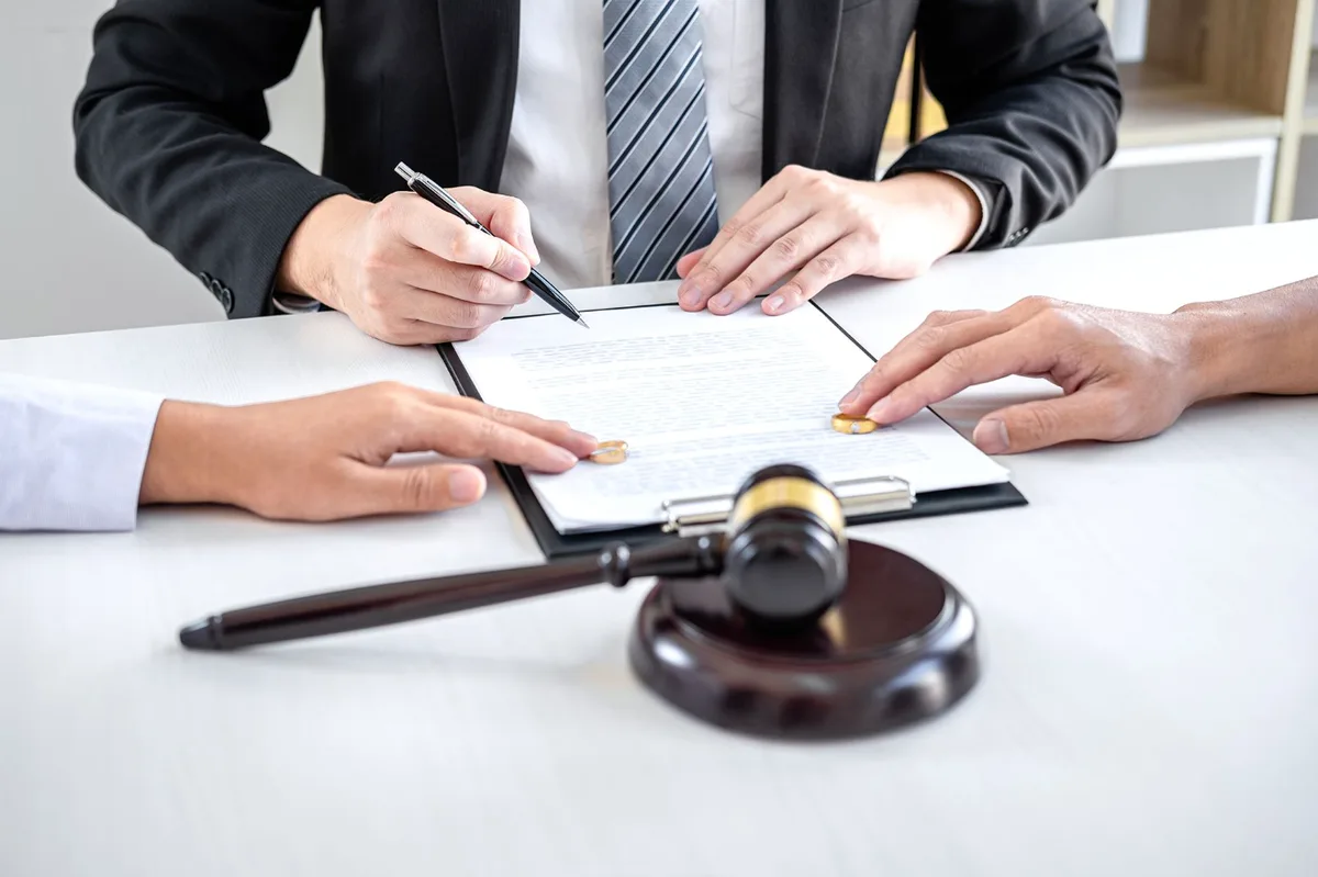Divorce agreement being signed at a table, gavel and rings in the foreground